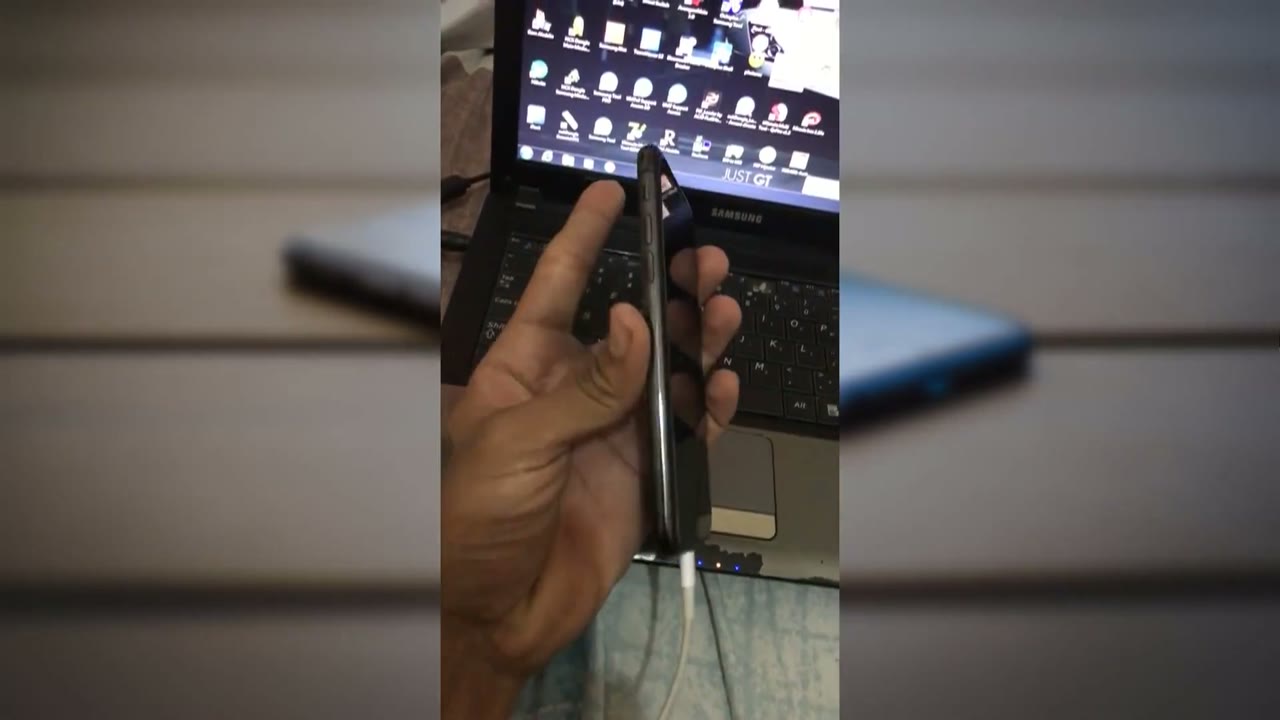 Mano presionando los botones del costado del iPhone X mientras está conectado a la computadora