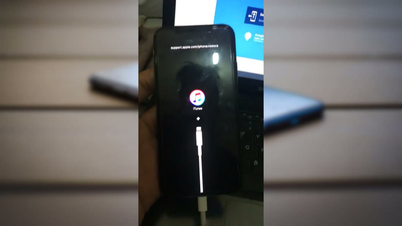 iPhone X atascado en modo recuperación, con el logo de iTunes y el cable en la pantalla, conectado a una computadora